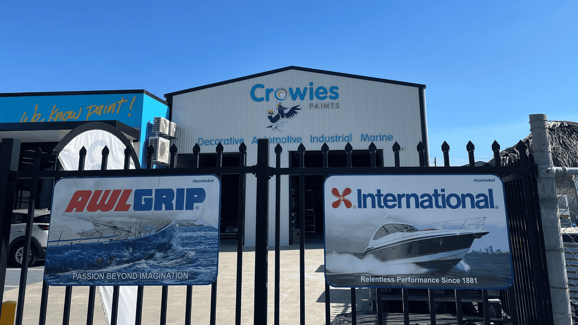 Exterior view of Crowies Paints building and entrance, with Awlgrip and International banners on the gate.