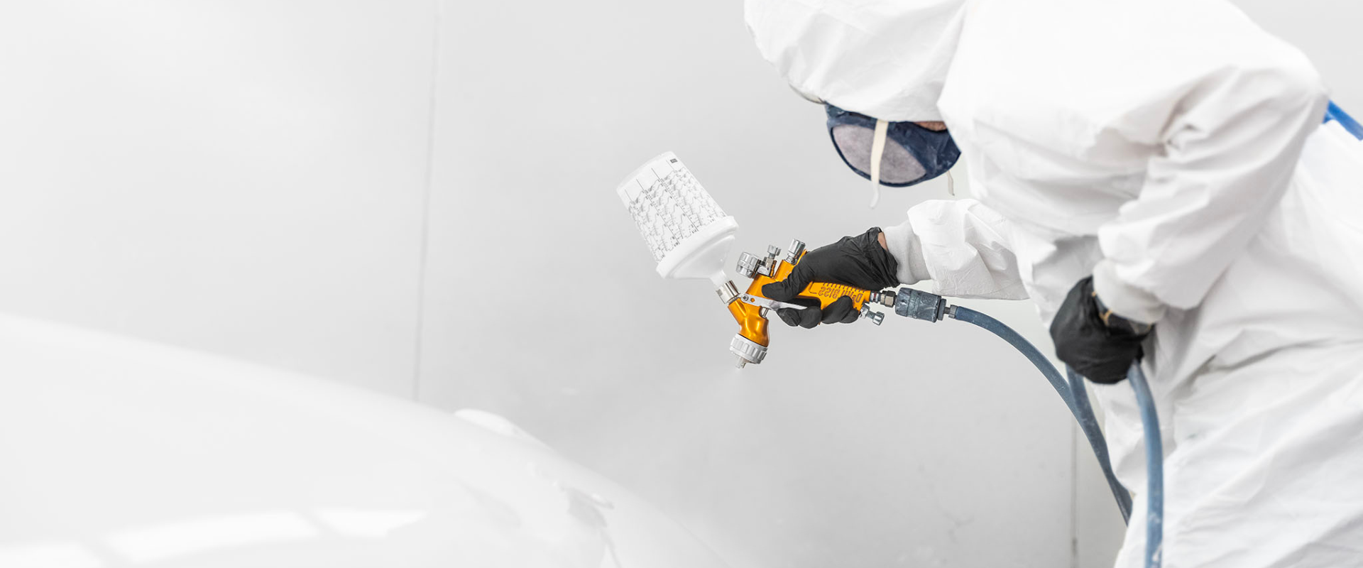 Professional applicator wearing PPE using a spray gun to apply high-gloss coating on a yacht surface in a spray booth