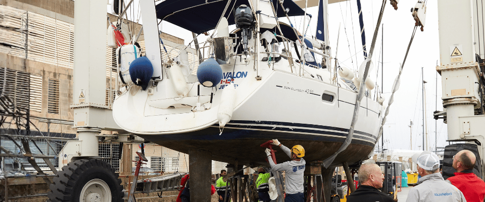 Sailing yacht Avalon lifted out of the water while workers apply coatings to the hull during a refit.