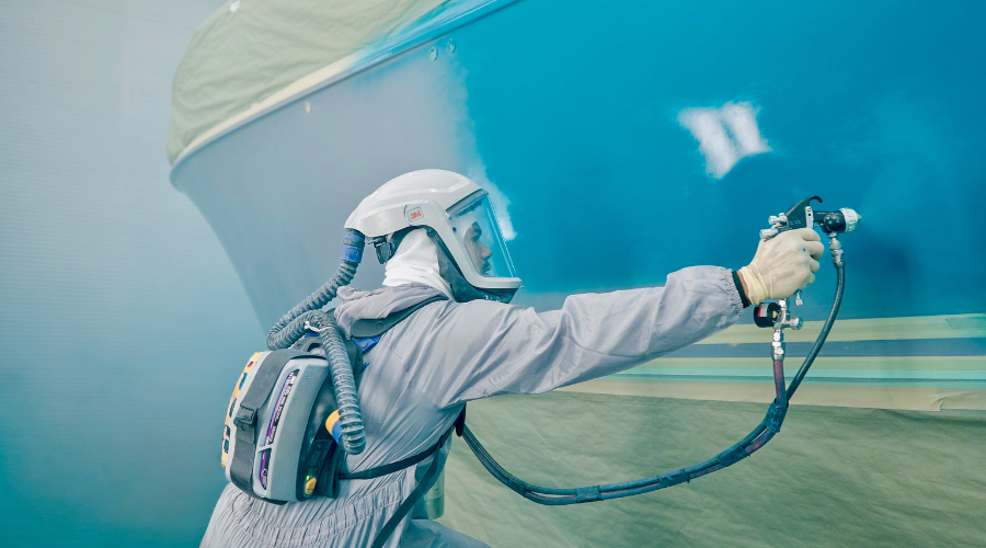 Applicator spraying an Awlgrip® coating onto the hull of a Hinckley yacht in a controlled spray booth.
